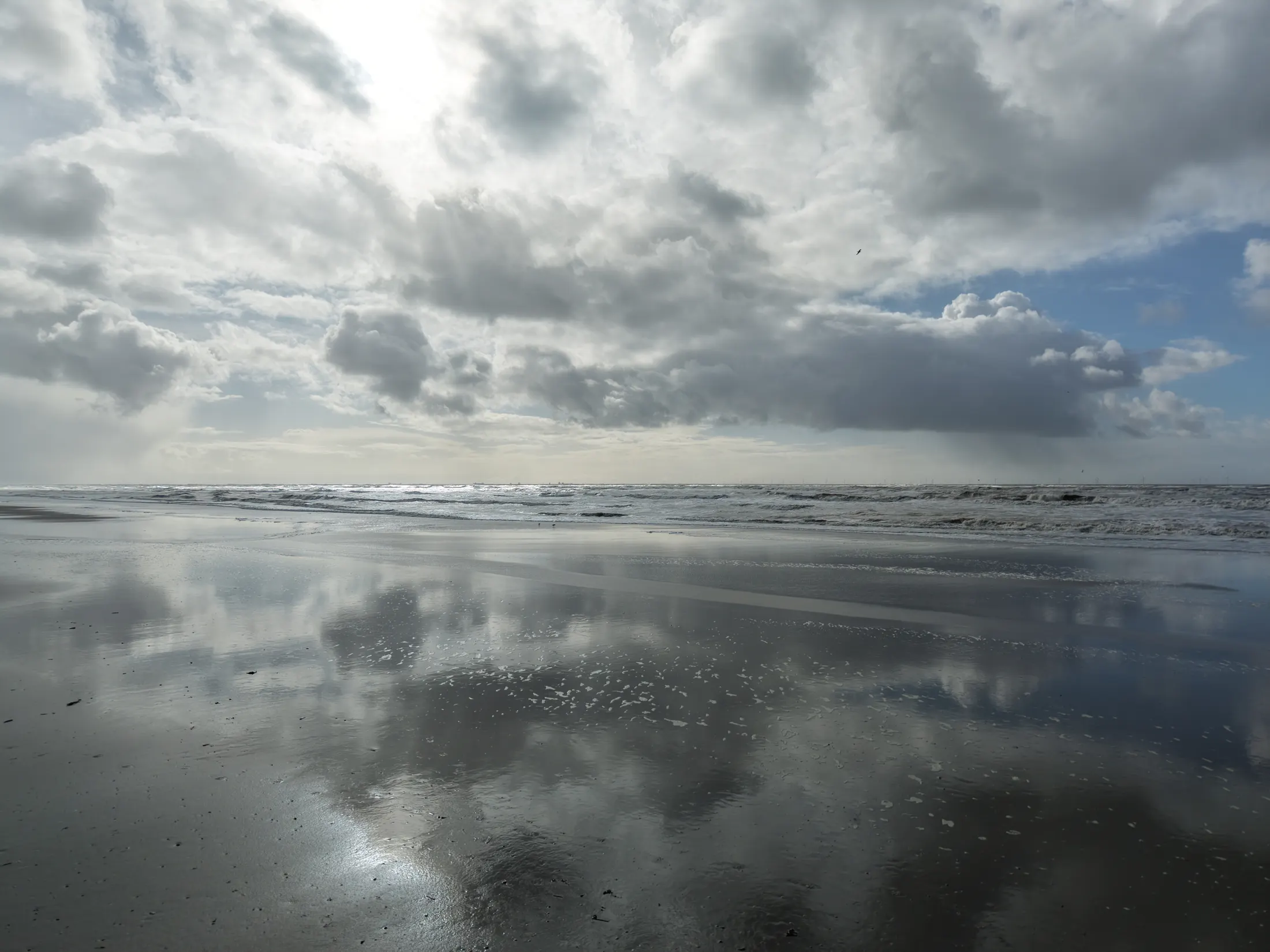 Dronebeeld van het strand van Noordwijk met de wolken weerspiegeld in het natte zand